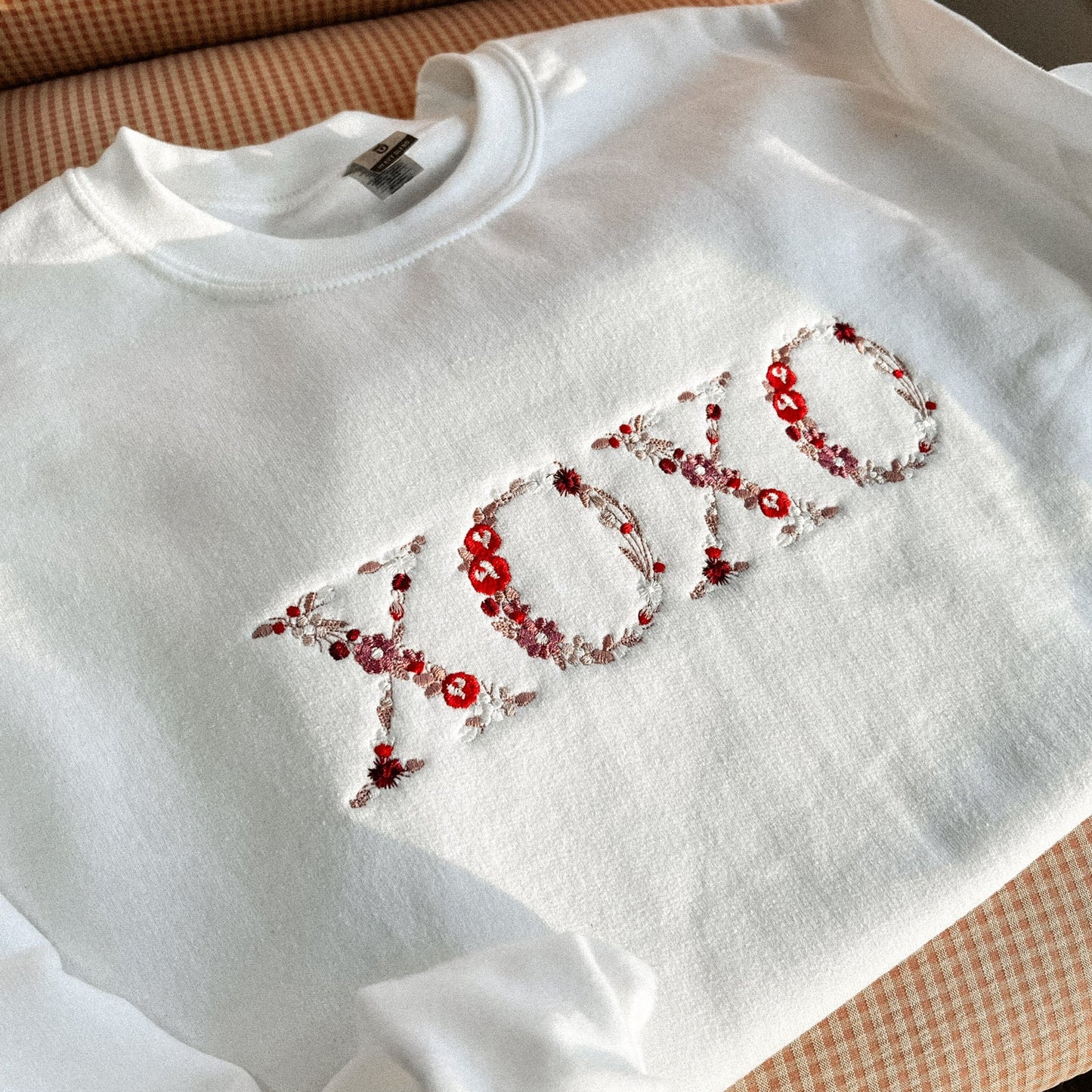 White sweatshirt with 'XOXO' embellished with red threads on a checkered surface.